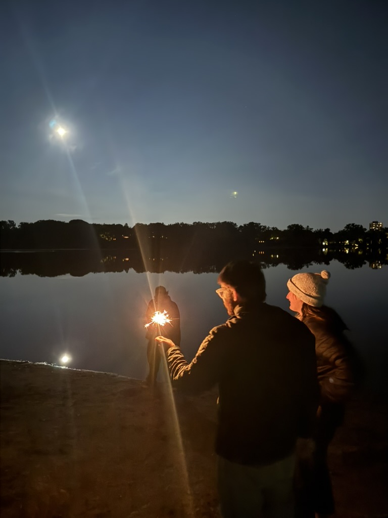 two people holding a sparkler by a lake under the moon